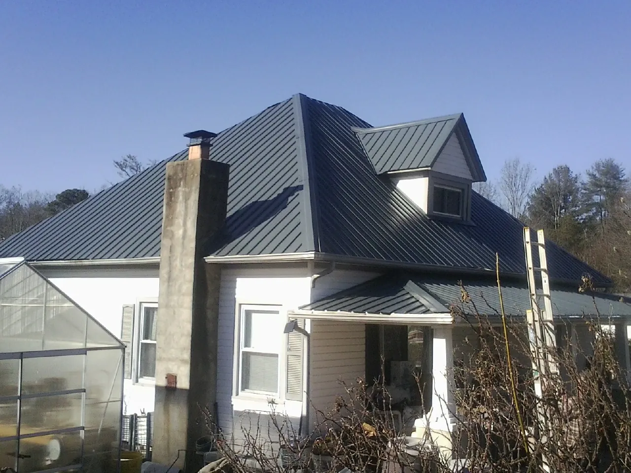 Dark blue standing seam metal roof on a white farmhouse with dormer — Slate & Tile Roof Repair by Roofing Brothers in Alplaus