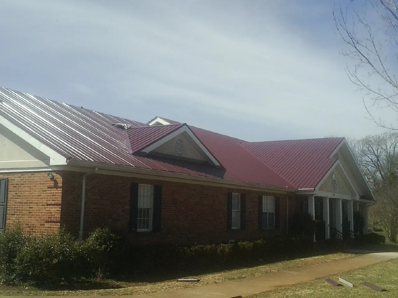 Red metal roof with gabled entries on a long brick building, from a Hail Damage Roof Repair job in Alplaus