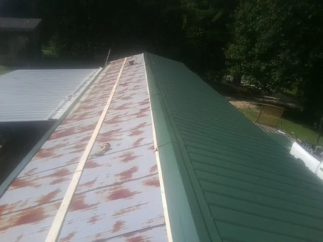 Old rusted panels beside newly installed green metal roofing — Wind Damage Roof Repair by Roofing Brothers in Alplaus