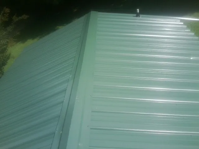 New green metal panels meeting at the ridge of a roof — Flat Roof Repair work by our crew in Alplaus