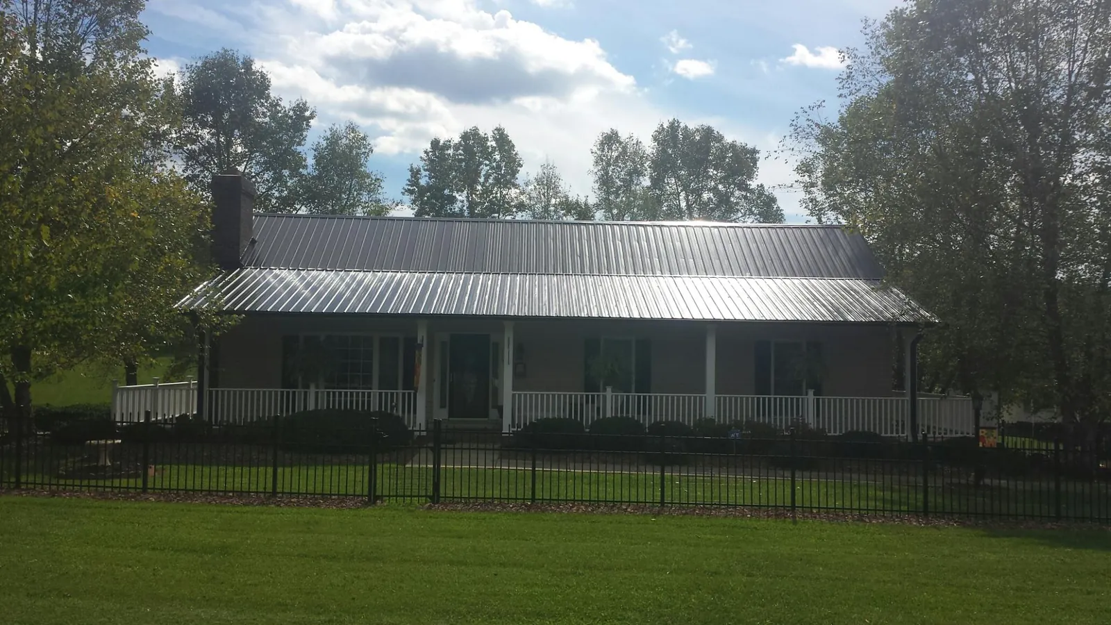Gray metal roof on a brick ranch with a full width front porch — Gutter Guard Installation work by our crew in Alplaus